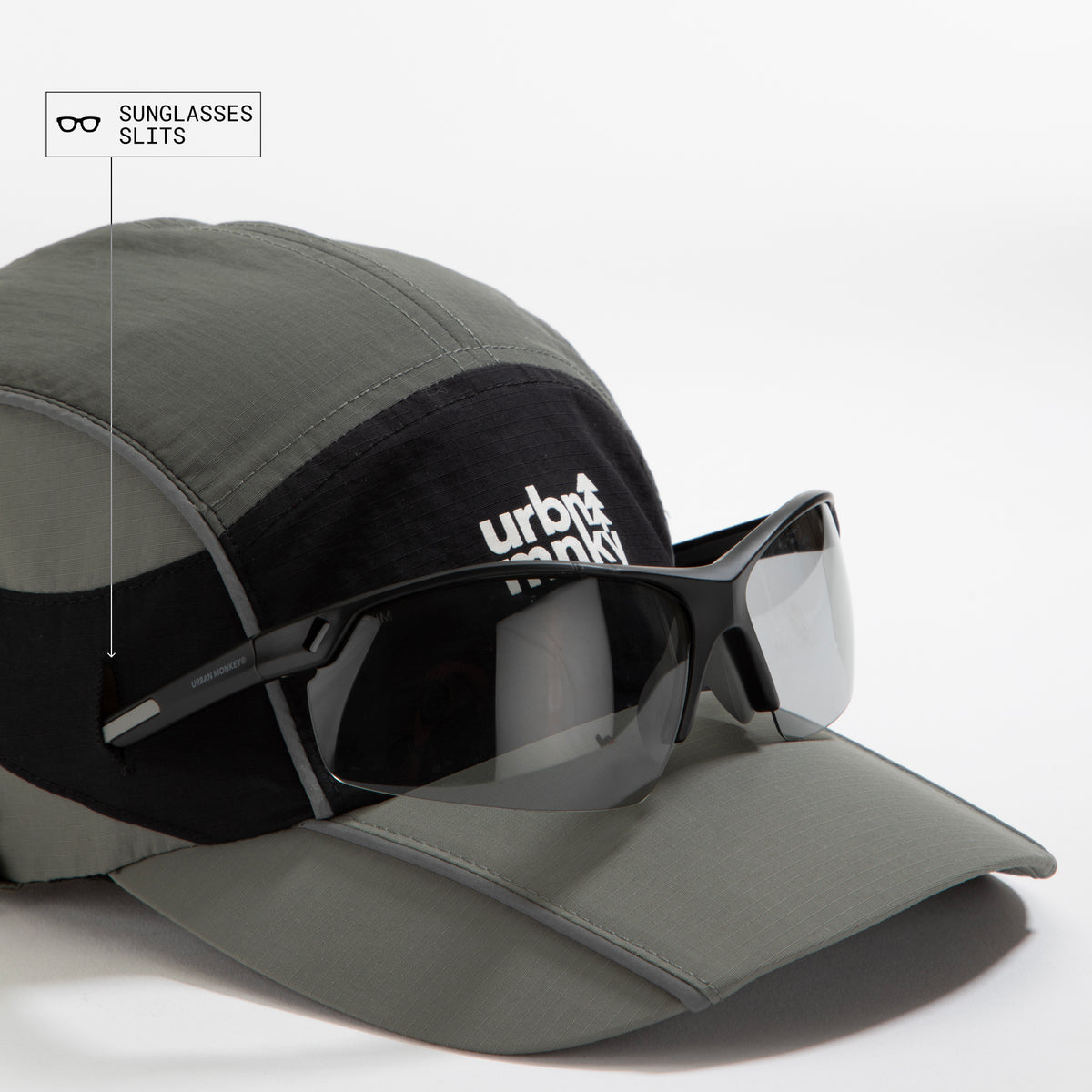 Side view of olive-grey and black color-block nylon cap with white stacked logo and pine tree icon and sunglasses slits. Urban Monkey®