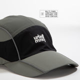 Side view of olive-grey and black color-block nylon cap with multi panel designed with white stacked logo and pine tree icon . Urban Monkey®