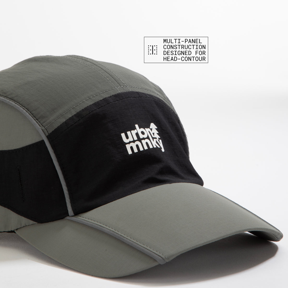 Side view of olive-grey and black color-block nylon cap with multi panel designed with white stacked logo and pine tree icon . Urban Monkey®