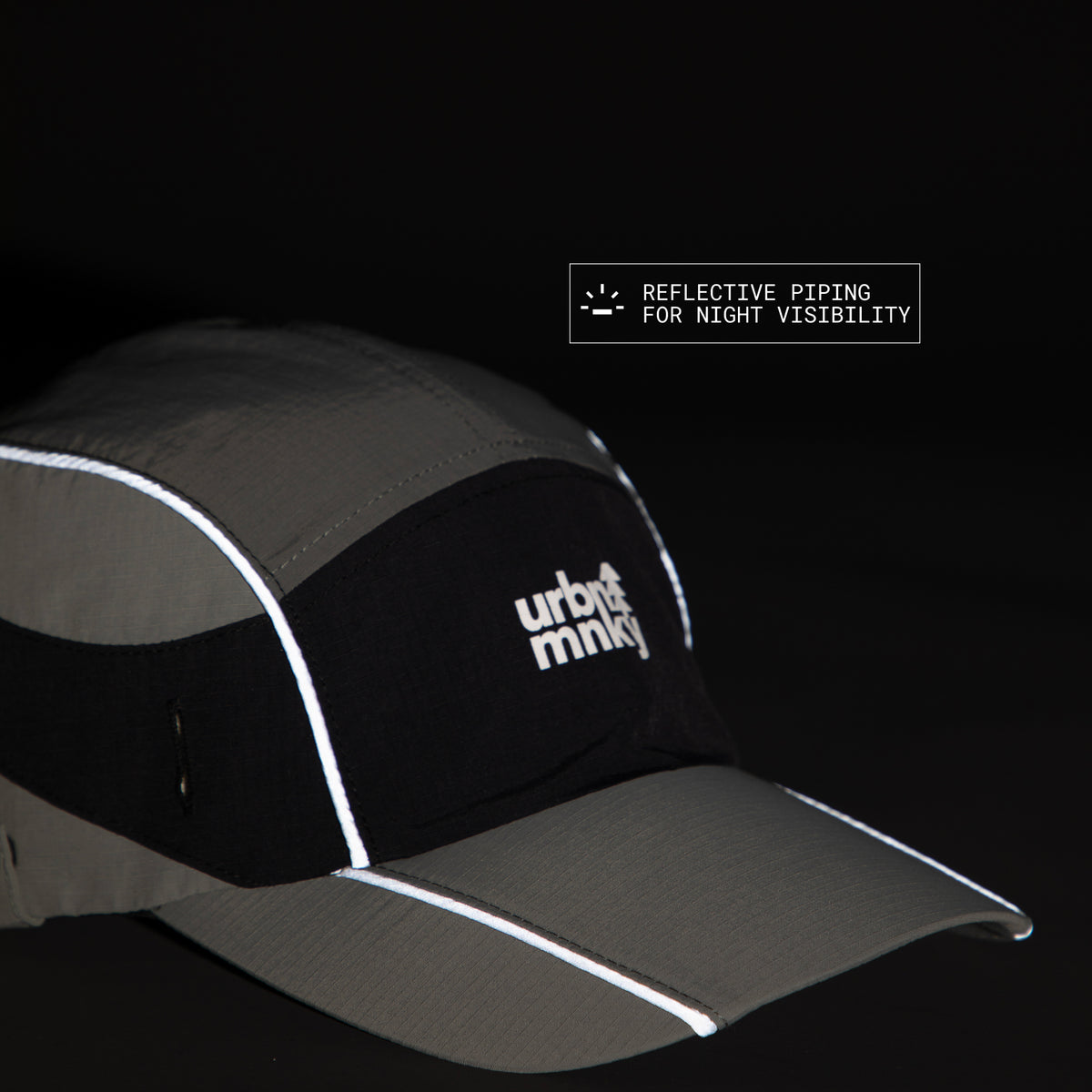 Side view of olive-grey and black color-block nylon cap with white stacked logo and pine tree icon and radium piping for night visibility. Urban Monkey®
