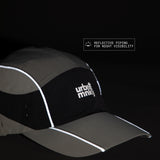 Side view of olive-grey and black color-block nylon cap with white stacked logo and pine tree icon and radium piping for night visibility. Urban Monkey®