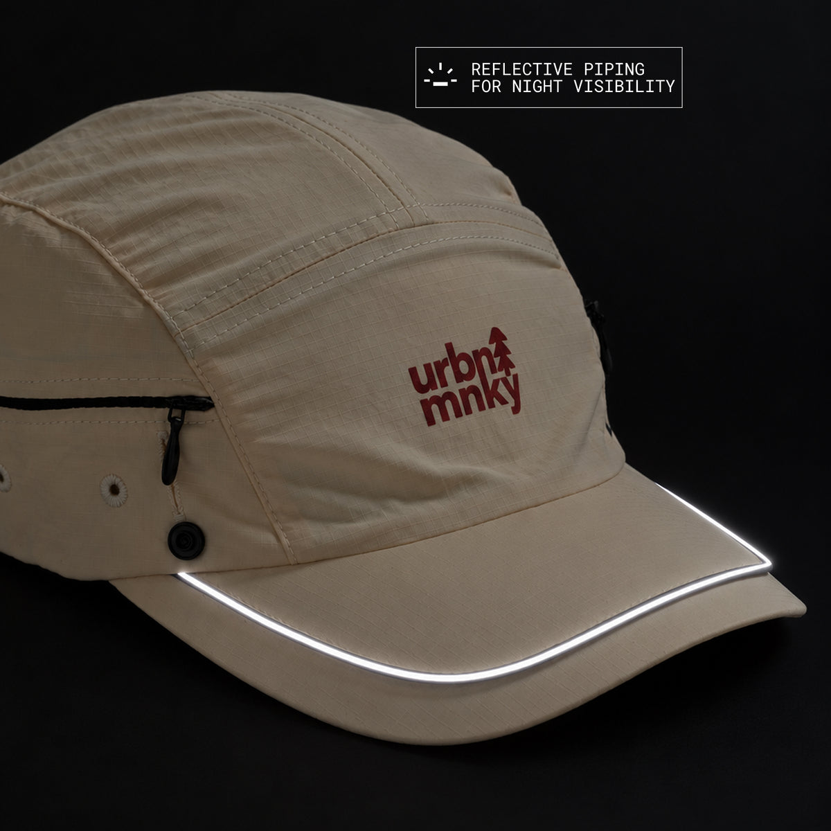 Front view of cream nylon sun cap with rust-red embroidered logo, zip pocket, and radium piping for night visibility. Urban Monkey®