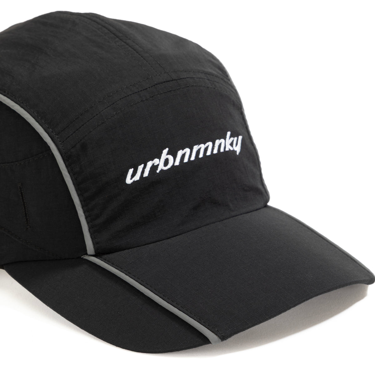 Front view of  black ripstop nylon cap with grey piping, sunglasses eyelet and white embroidered logo Urban Monkey®