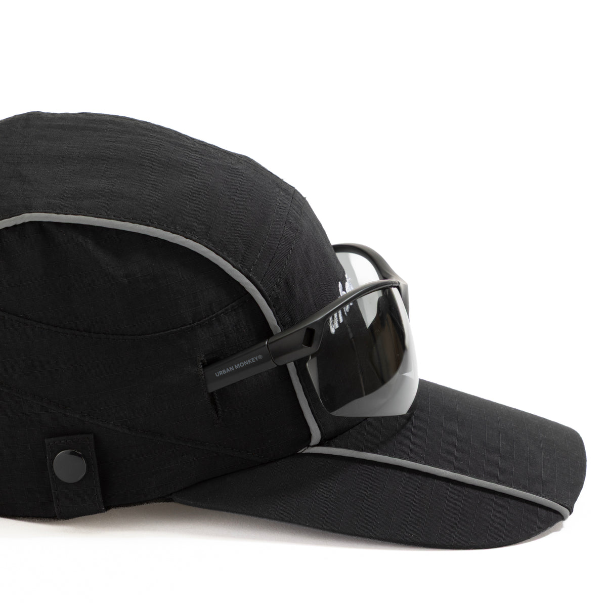 Side view of black ripstop nylon cap with grey piping, sunglasses eyelet, white embroidered logo and metal side clips Urban Monkey®