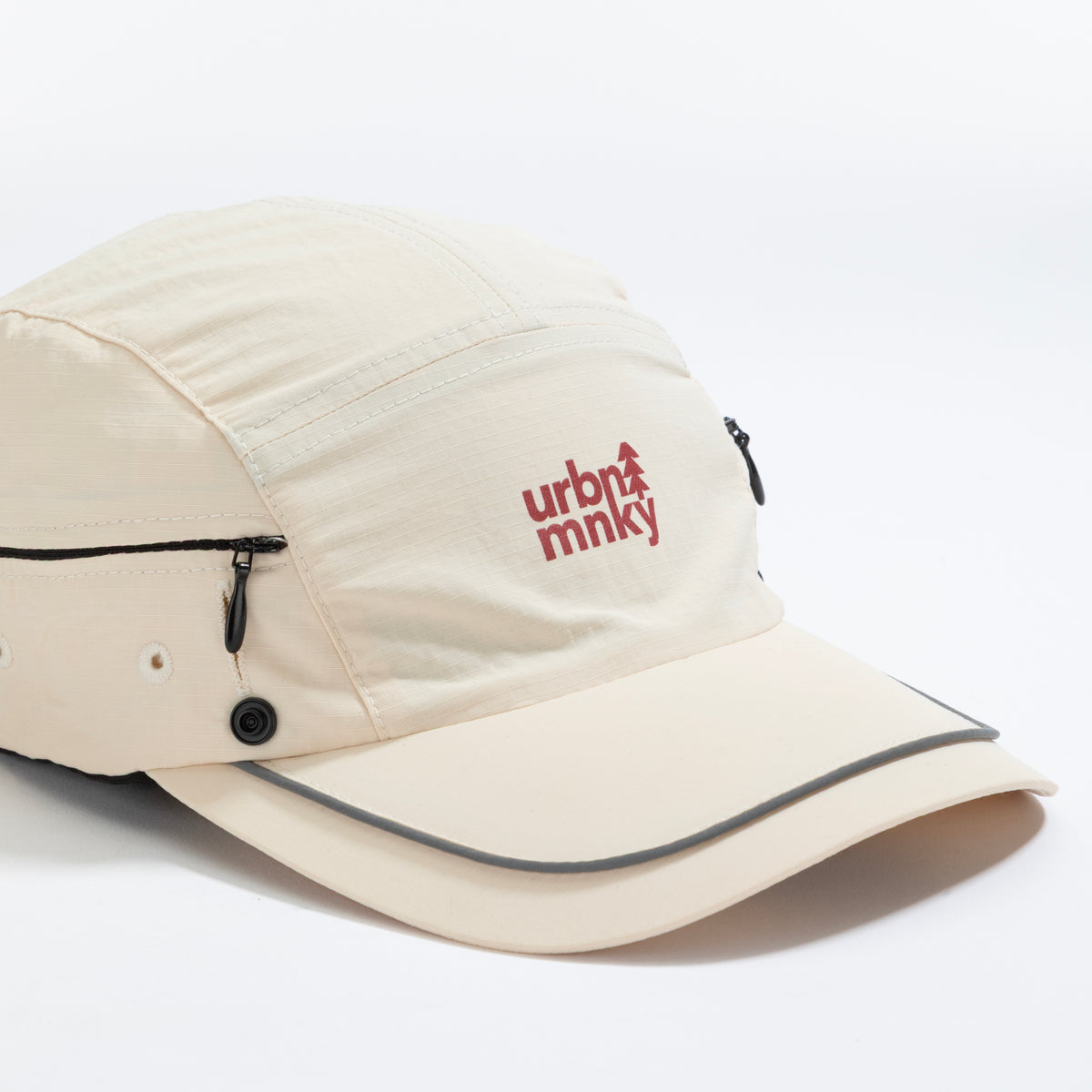 Front view of cream nylon sun cap with rust-red embroidered logo, zip pocket, and snap button. Urban Monkey®