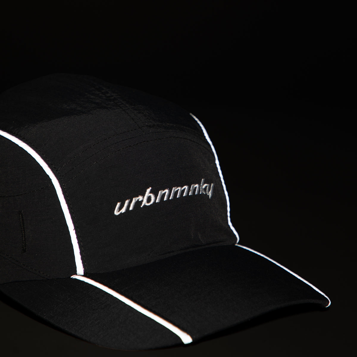 Front view of black ripstop nylon cap with grey piping, sunglasses eyelet white embroidered logo Urban Monkey®