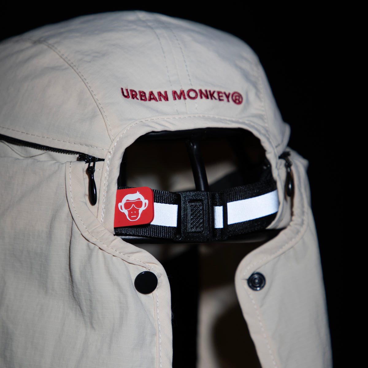 Back view of cream nylon sun cap with red embroidered logo, zip pocket and adjustable strap,. Urban Monkey®