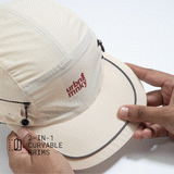 Front top view of cream nylon sun cap with rust-red embroidered logo, zip pocket, and flexible panel. Urban Monkey®